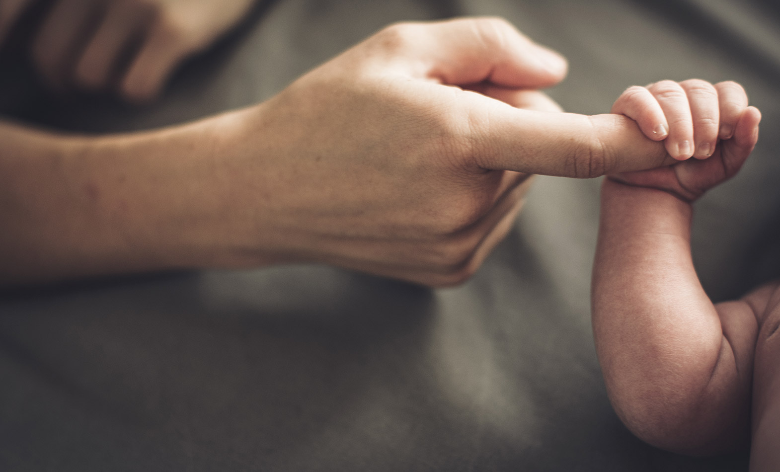 Foto von einer Mutter deren Finger von einer Babyhand umklammert wird.
